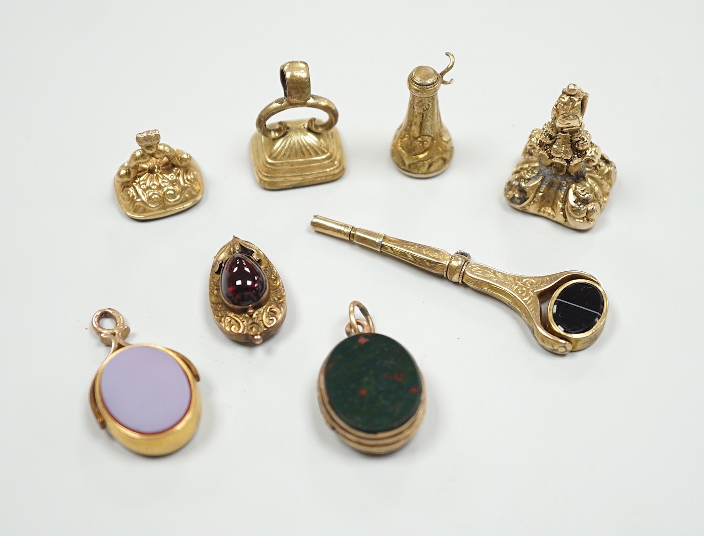 Four assorted 19th century and later yellow metal overlaid and gem set fob seals, a Victorian 15ct gold and sardonyx spinning fob, a sardonyx set locket, damaged pendant and yellow metal and two stone set watch key.